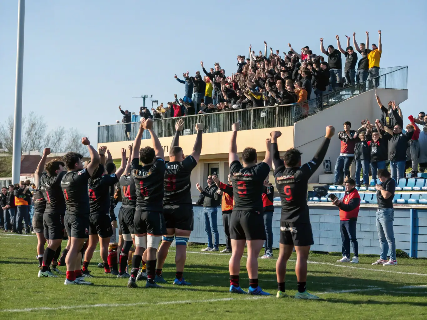 A group of young rugby players in USJO UNION SPORTIVE JUILLAC jerseys, celebrating a victory with their coaches on a sunny field. The image conveys teamwork, joy, and the spirit of sportsmanship.